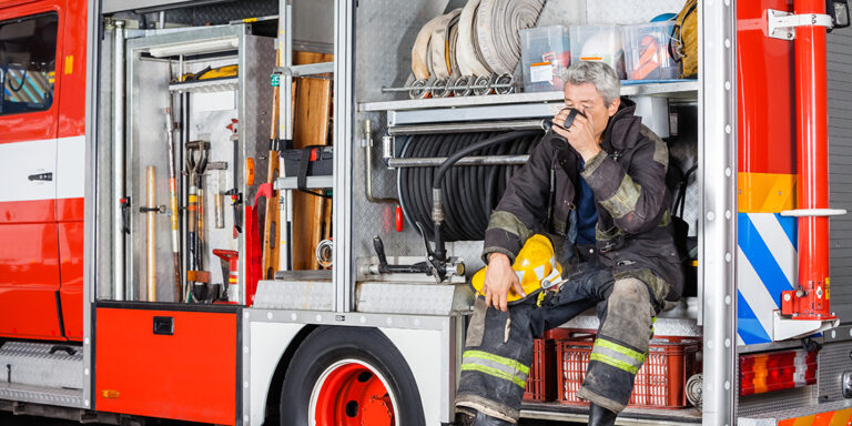 Full length of fireman drinking coffee while sitting in truck at fire station