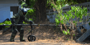 EOD officer in the explosive ordnance disposal suit using remote robot hand to check the unclear box beside the wall