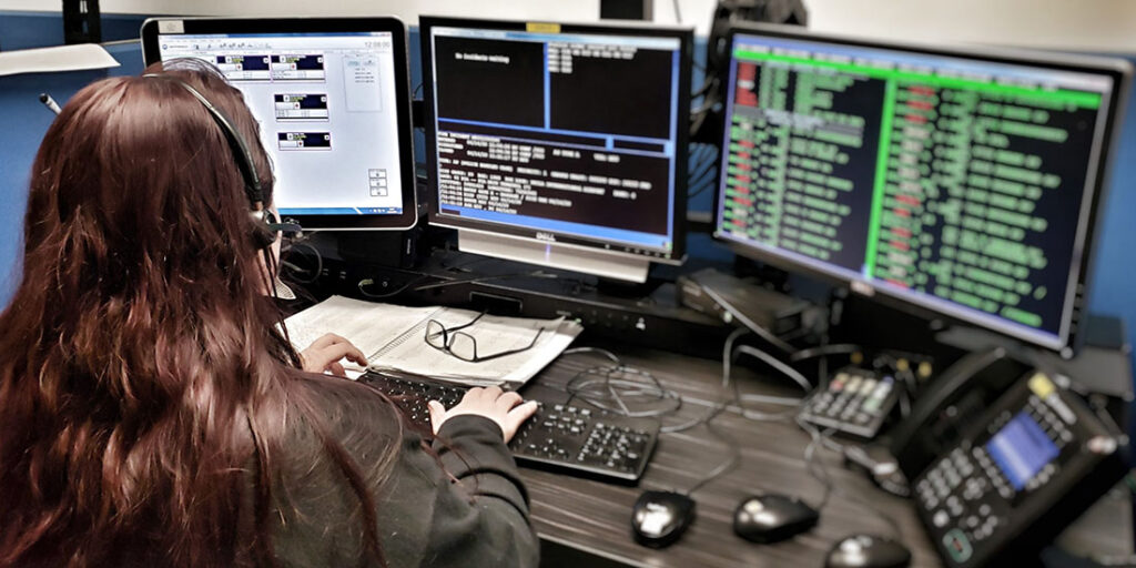 back of female 911 operator in front of multiple screens