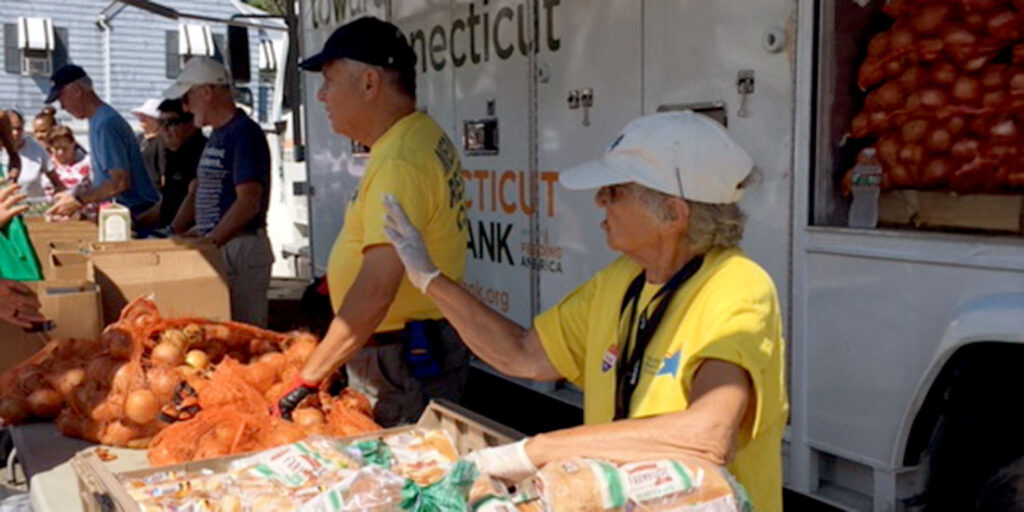Volunteers giving out food, such as bread and onions, outdoors under an awning