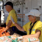 Volunteers giving out food, such as bread and onions, outdoors under an awning
