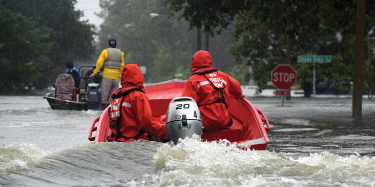 Coast Guardsmen in an inflatable motor boat motoring down a flooded street